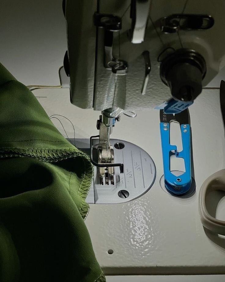 Close-up of a sewing machine with a green fabric and blue trimmers.